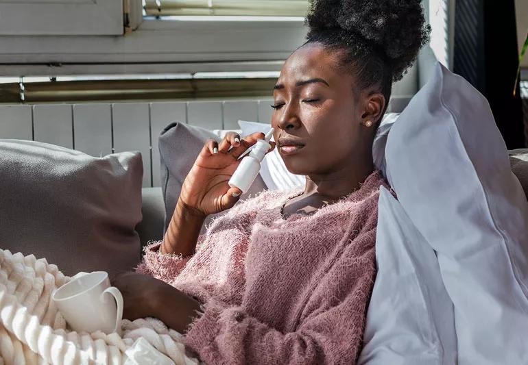 Person reclining on couch using nasel spray to alleviate pressure in sinuses.