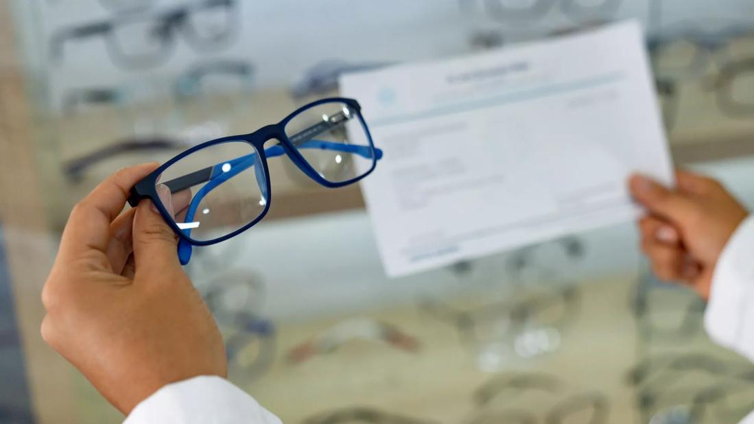 Eye doctor holding glasses and a prescription