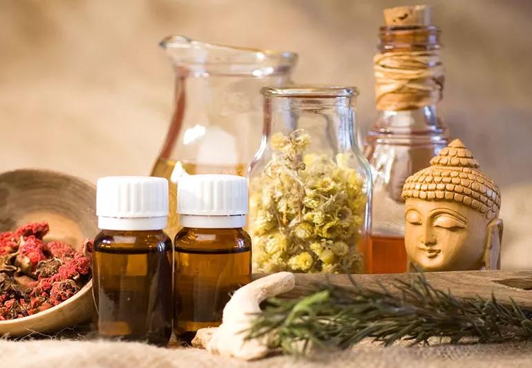 Herbs, tinctures and other bottles sit next to a small statue on a cloth-covered table.