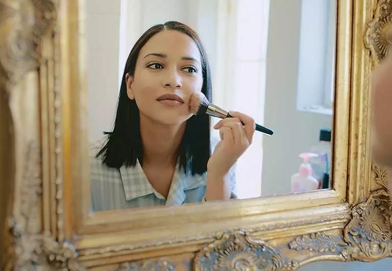 person applying makeup foundation in mirror