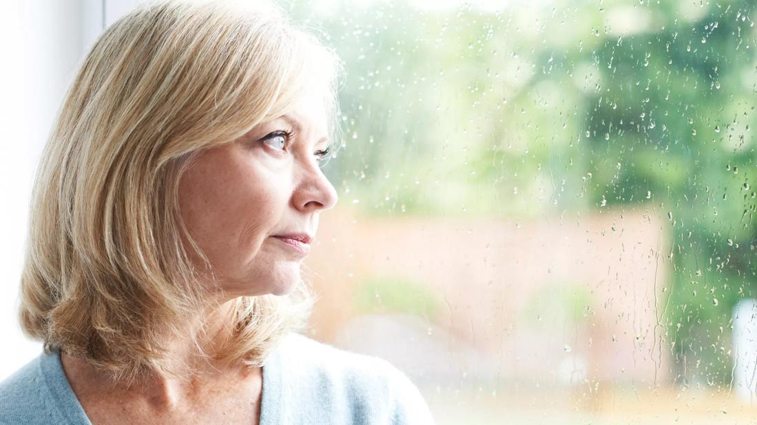 An forlorn individual looks out a window on a rainy day