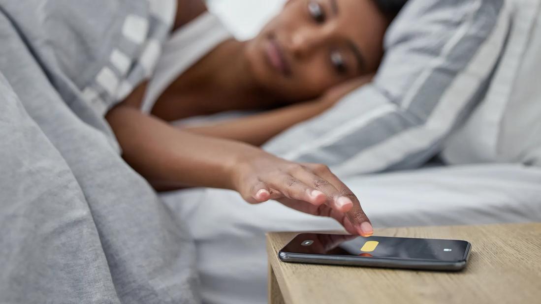 Person in bed hitting snooze on their cell phone