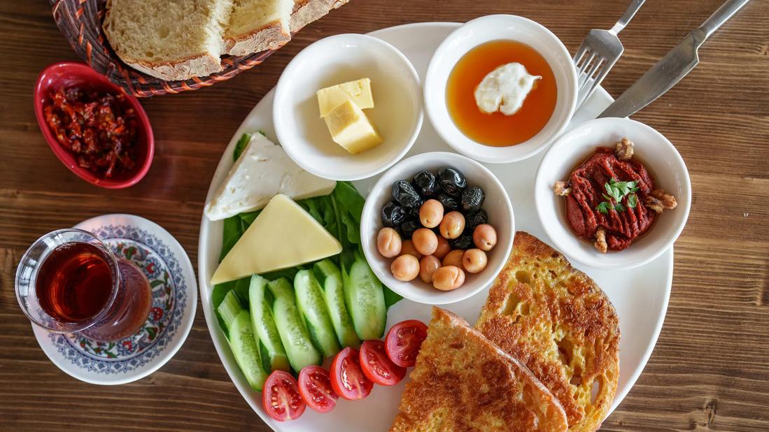 Plate full of an array of snack foods like vegetables, fruits, nuts, pickles, cheese and bread