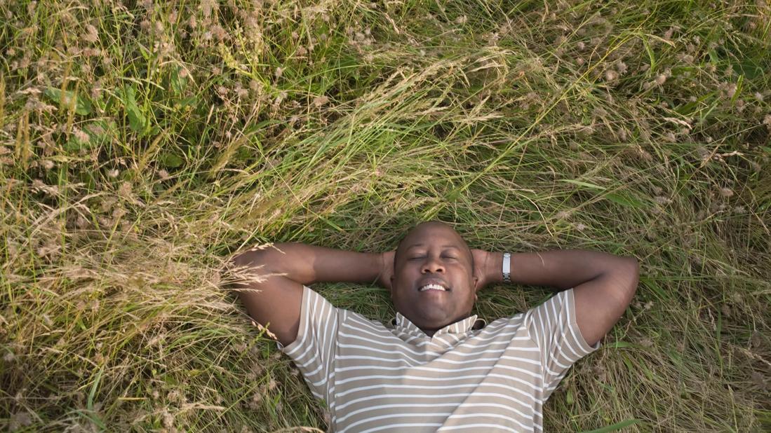 Person smiling, lying back, eyes closed, relaxing in long grass