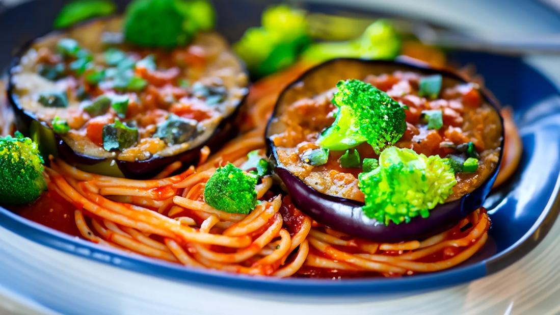 Cooked eggplant halves over marinara pasta and cooked broccolini