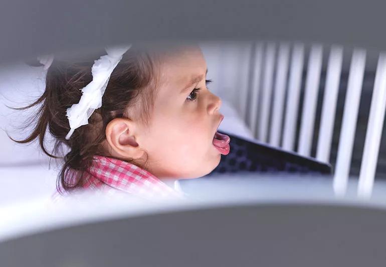 Baby coughing in white crib.