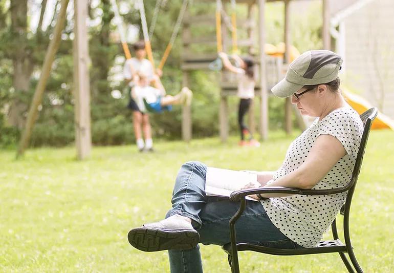 woman reading in backyard while kids play