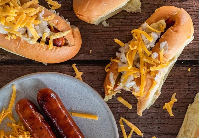Tofu turkey hotdogs sit on a plate and in hotdog buns covered in diced onions and cheese.