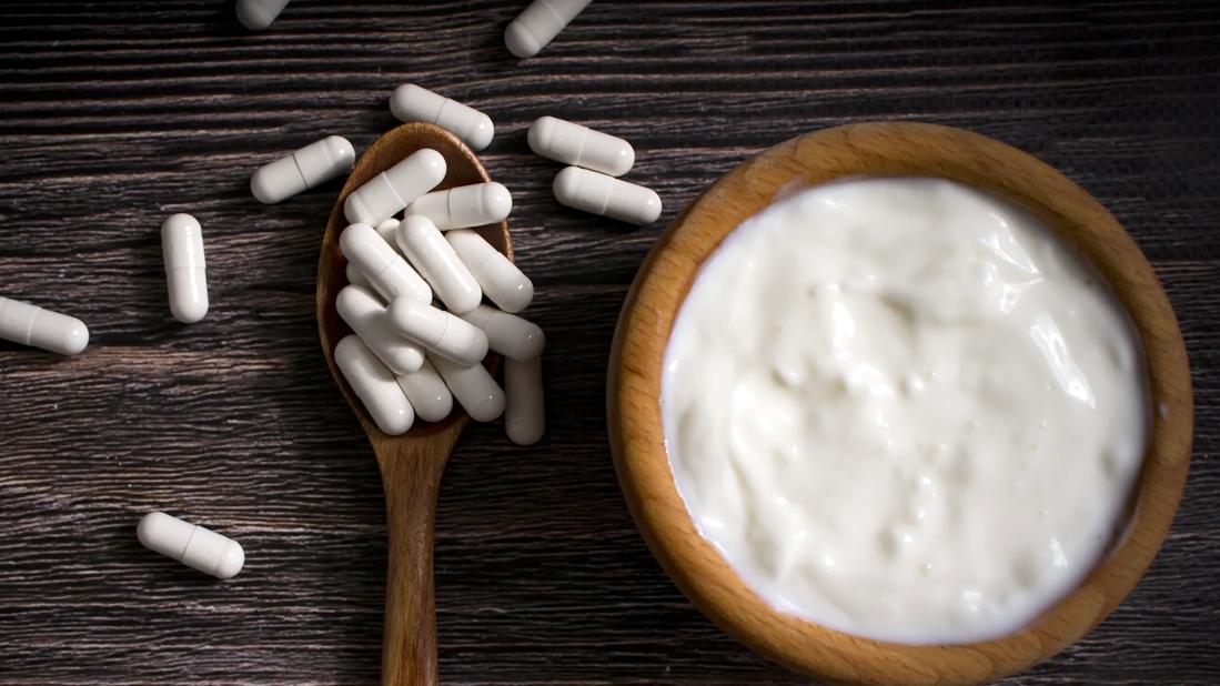 Wooden bowl of white yogurt next to wooden spoon of white capsules