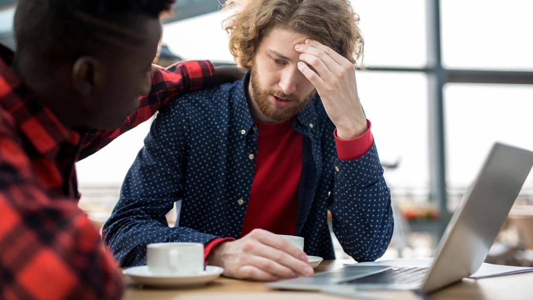 Person comforting stressed out person, with coffee cups and open laptop on table