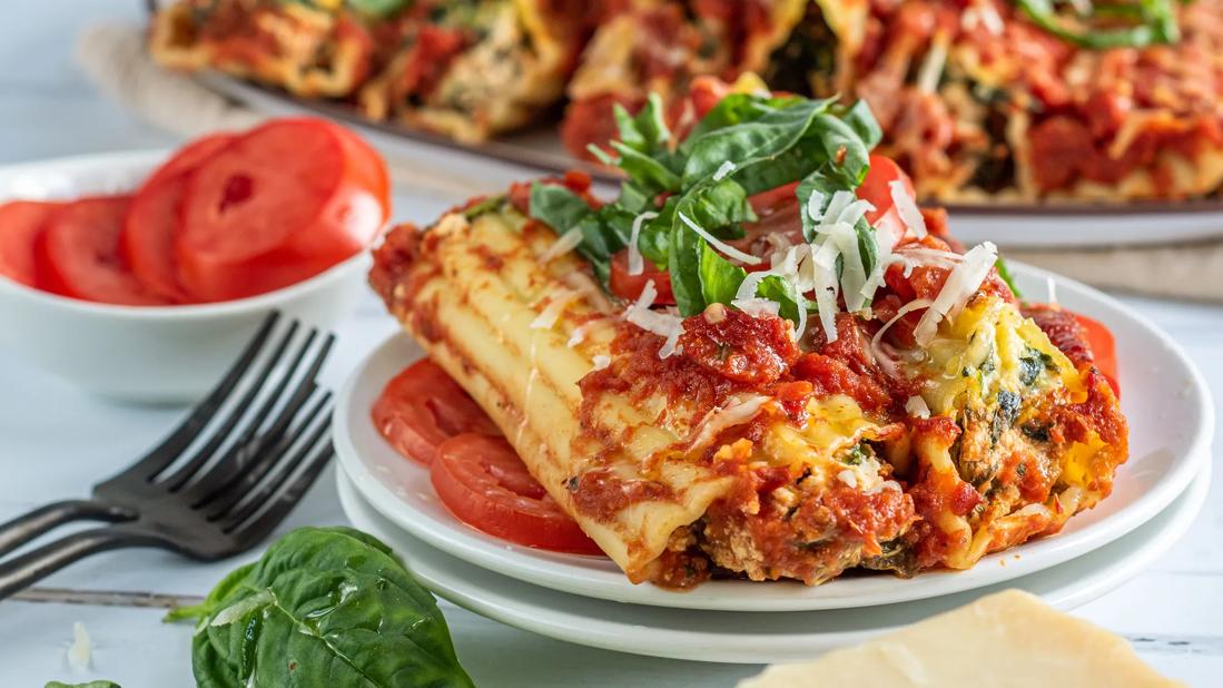 Two tofu-stuffed manicotti displayed on a bed of sliced tomatoes