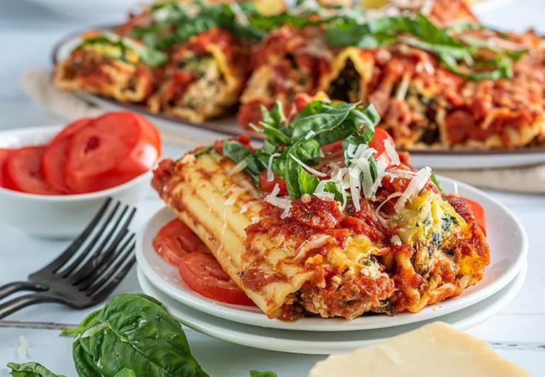 Two tofu-stuffed manicotti displayed on a bed of sliced tomatoes