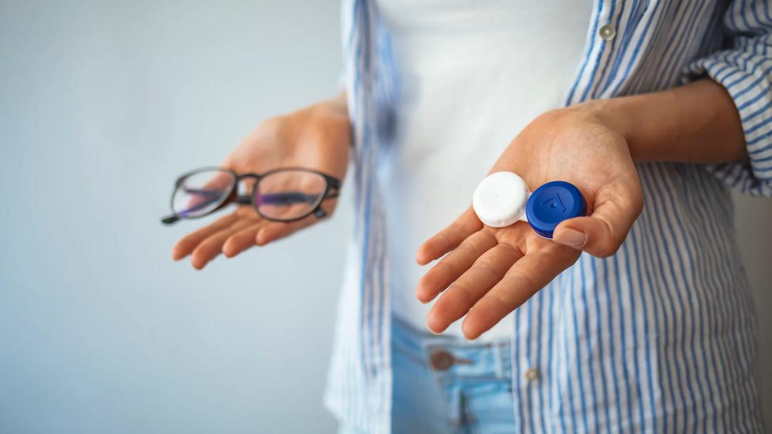 Person holding contact lenses case in one hand and glasses in the other hand