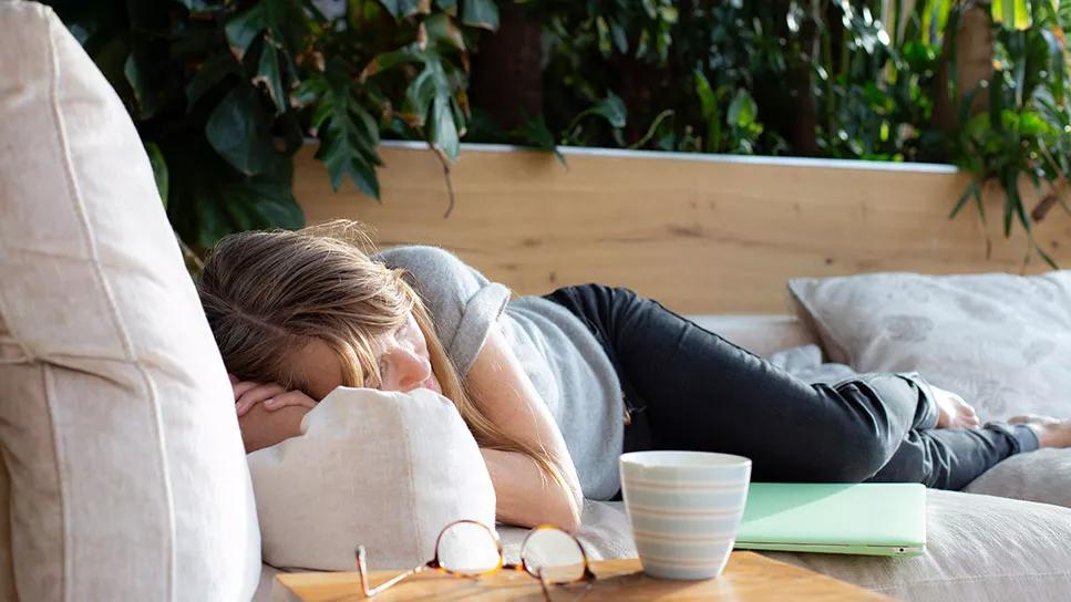 Female asleep on couch on backyard deck next to laptop and glasses