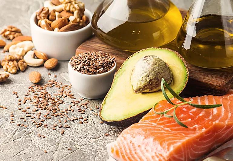 Raw salmon is displayed next to an avocado, various nuts and bottles of olive oil.