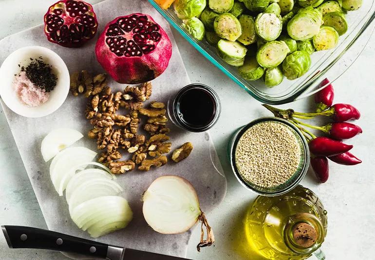 Dish of uncooked Brussels sprouts sits alongside a cutting board with apple-pecan slaw ingredients