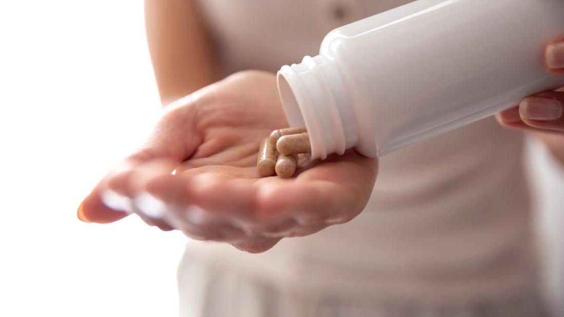 Hand pouring capsules out of white bottle into other hand