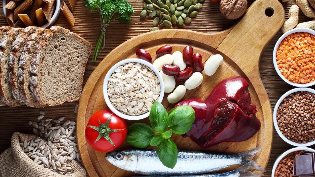 An array of copper-rich foods on wooden board, inlcuding liver, sardines, legumes and seeds