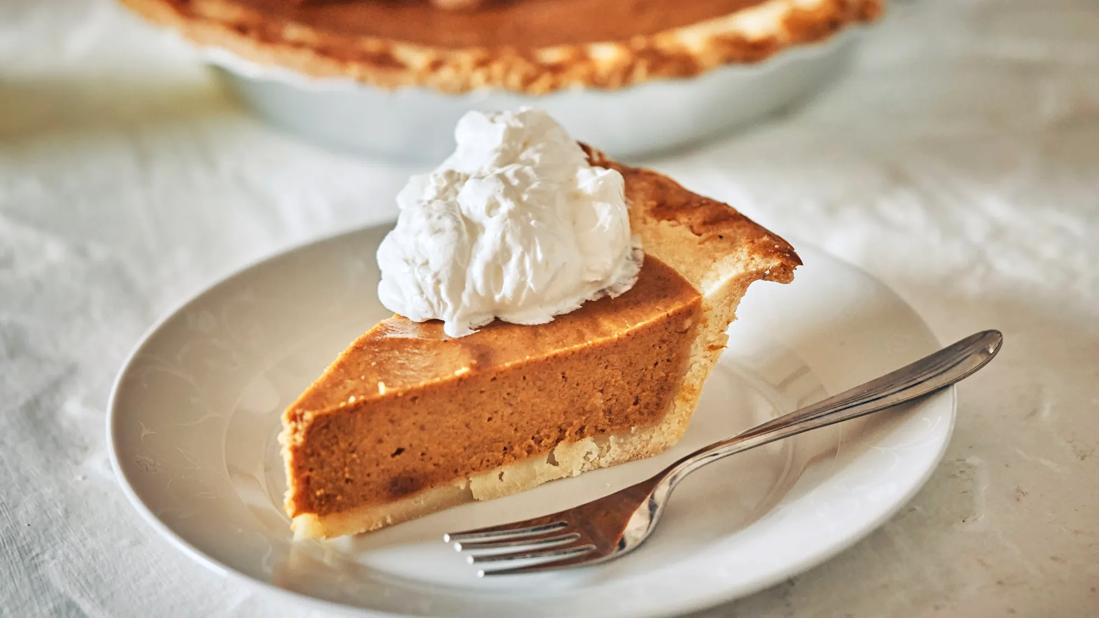 Slice of pumpkin pie with dollop of whipped topping on white plate with fork