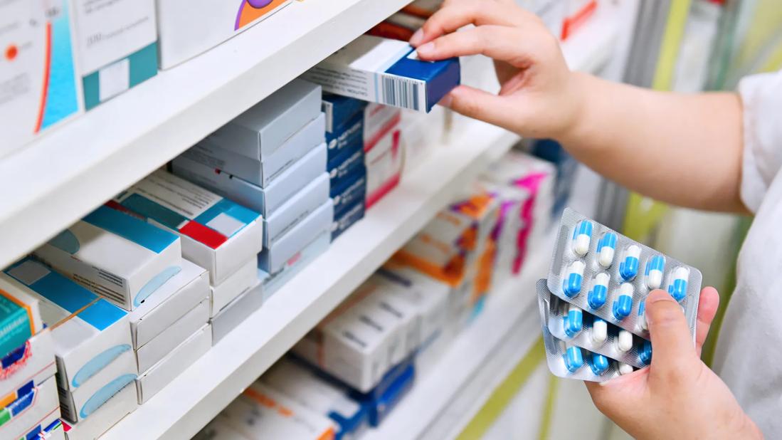 Hands selecting medicine from shelves of medicines