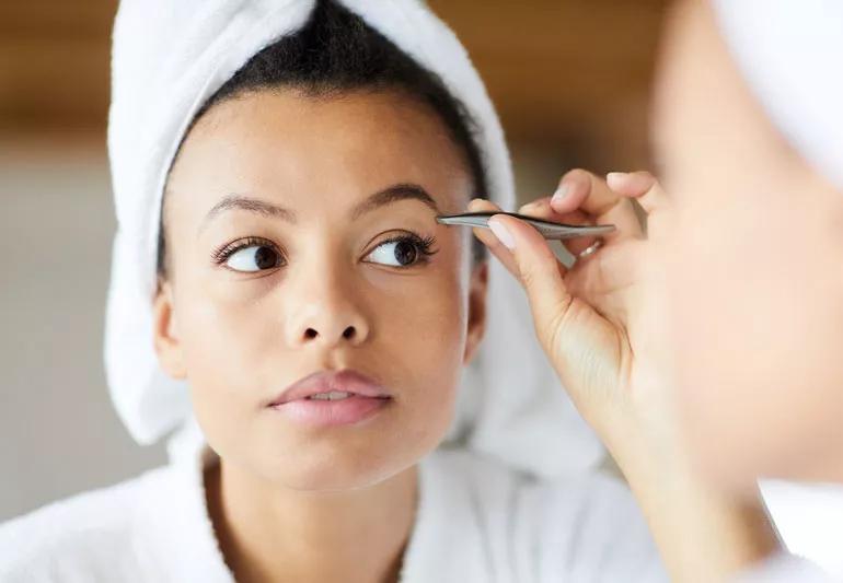 Woman is plucking her eyebrows after shower