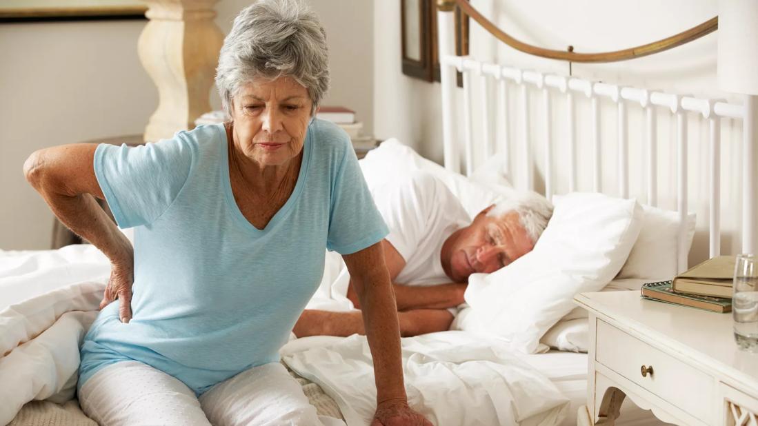 A senior woman suffering from a backache getting out of bed.