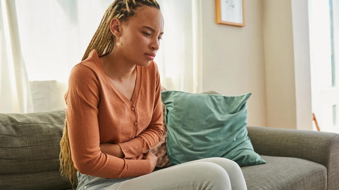 Person sitting on couch with arms around stomach, grimacing