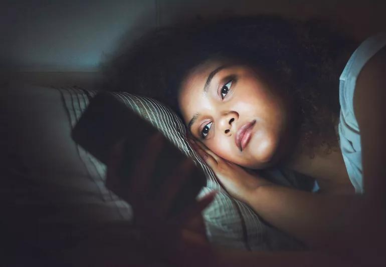 Young woman with smartphone in bed at home bedroom