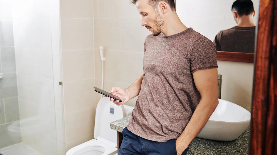 Man leaning against sink in the bathroom on their phone