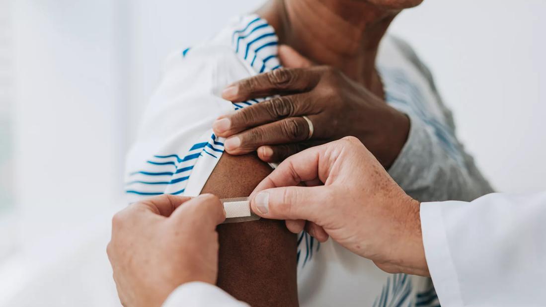 Healthcare provider placing bandaid on upper arm after a shot