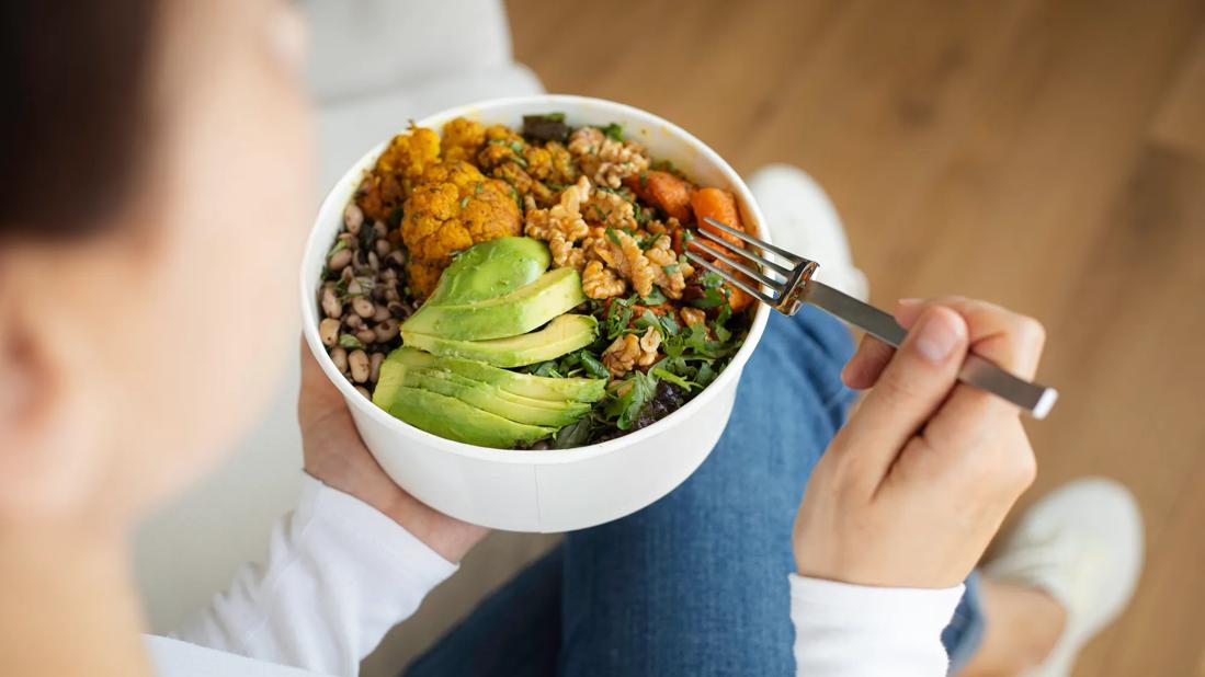 Person holding bowl of healthy grains, beans, avocado and other vegetables