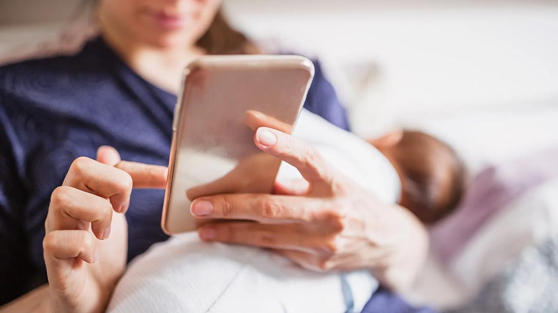 Mother using phone while holding newborn