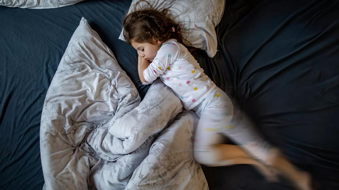 Child in pjs sleeping in bed moving legs