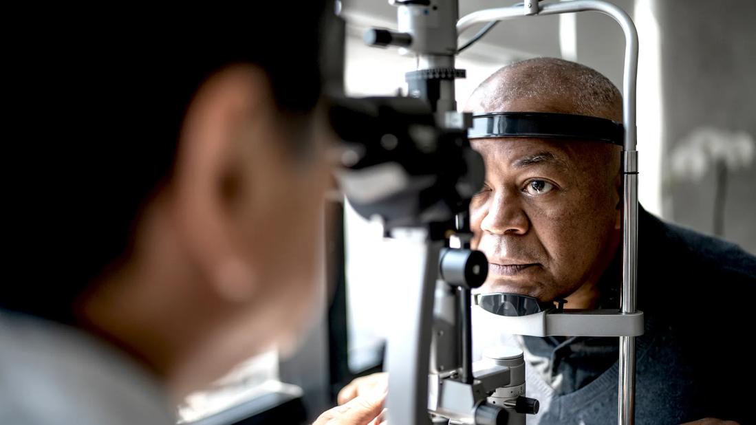 Person with head against eye exam equipment, with provider looking through other end at eyes