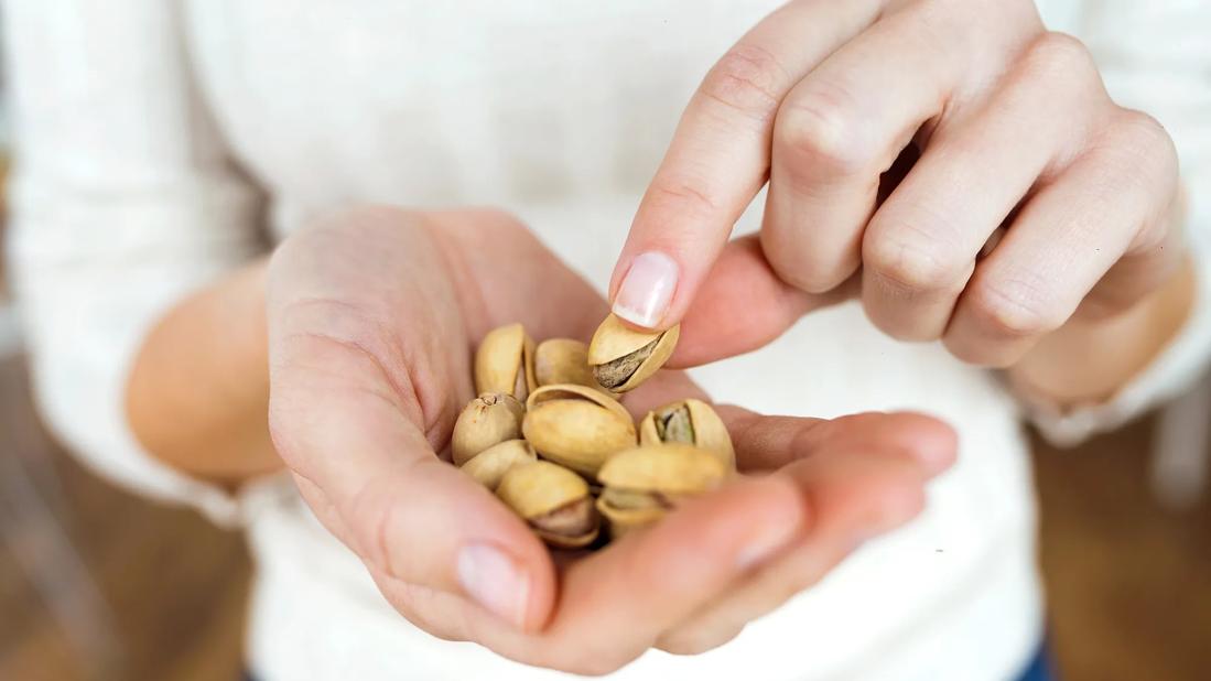 Hand holding pile of pistachios, with other hand picking one up