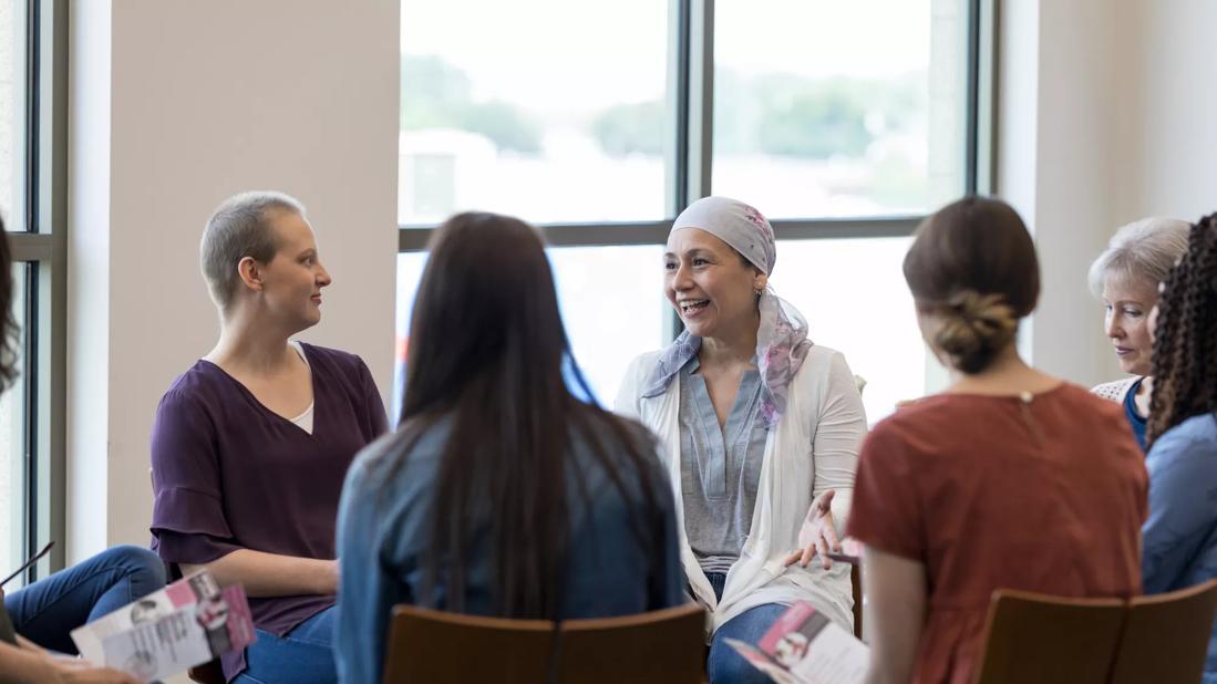 Group of women sitting in chairs in circle, some holding brochures, at cancer support group