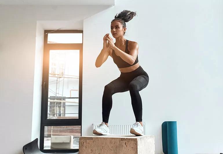 Person in workout clothing performs a box jump in a gym