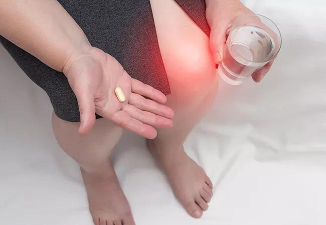 A woman with a sore knee holds a chondroprotector tablet and a glass of water, glucosamine and chondroitin sulfate in her hand, copy space