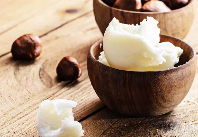 Shea butter and the nuts it is made from displayed on a wooden table.
