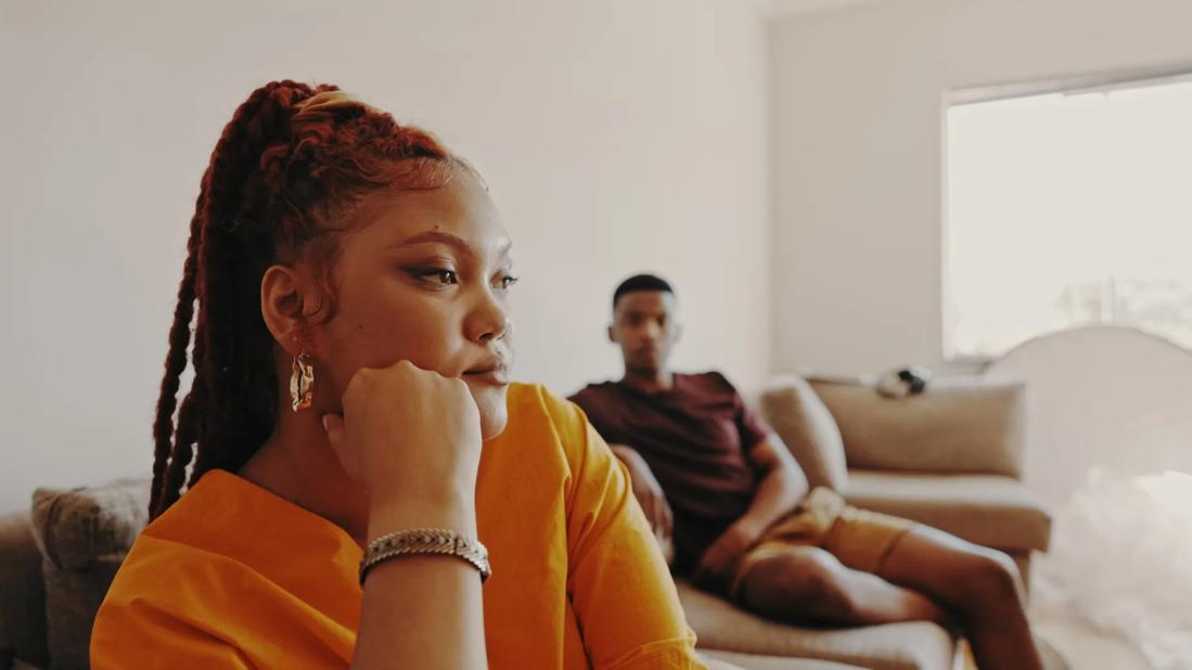 Person sitting defiantly with hand on chin, separate from other person on couch