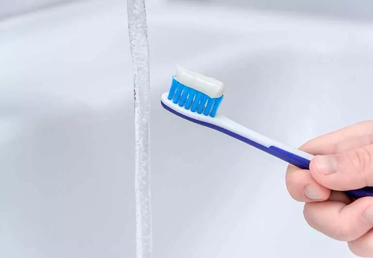 Toothbrush near bathroom sink faucet with water on.