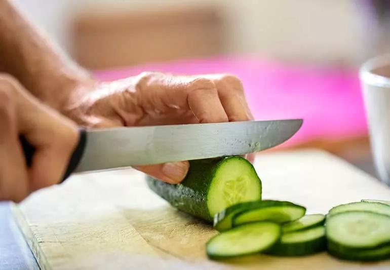 Person chopping a cucumber on cutting board.