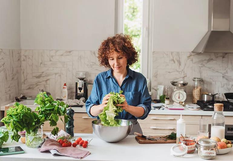 Person putting salad in a metal bowl in a kitchen setting