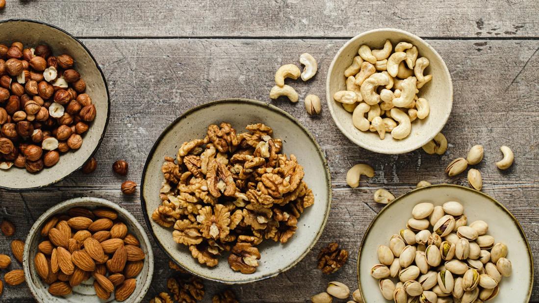 Separate bowls of shelled almonds, walnuts, cashews, hazelnuts, and in-shell pistachios