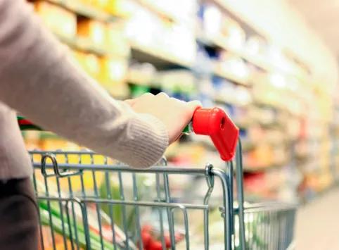 Close-up of a shopping cart being pushed down the aisle in a grocery store