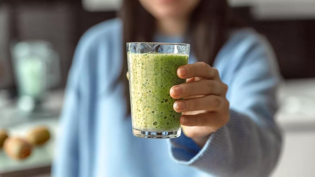 Person holding up glass of green-colored smoothie