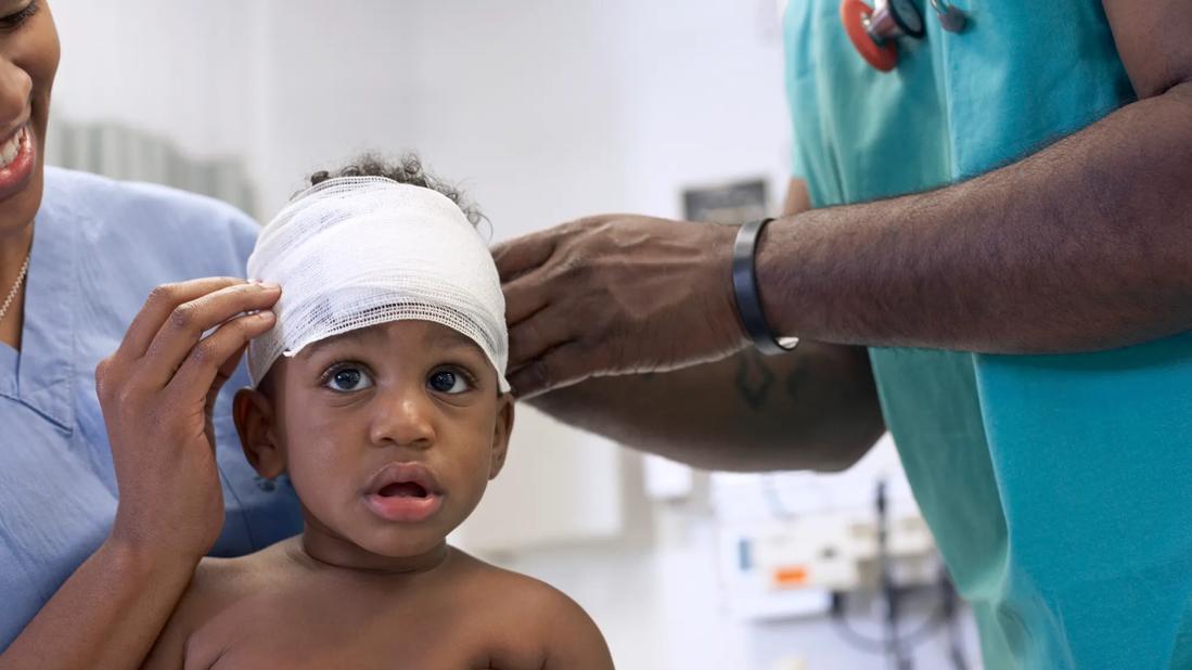 Toddler getting their head wrapped in bandage by two healthcare workers