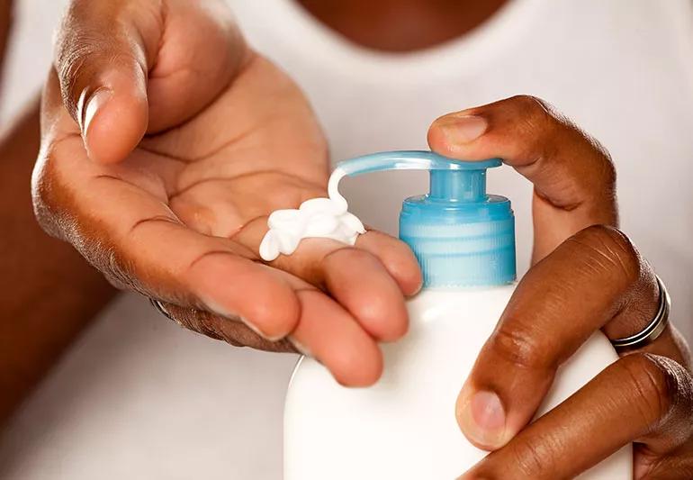 Closeup of hands pumping lotion from the bottle to use on dry skin