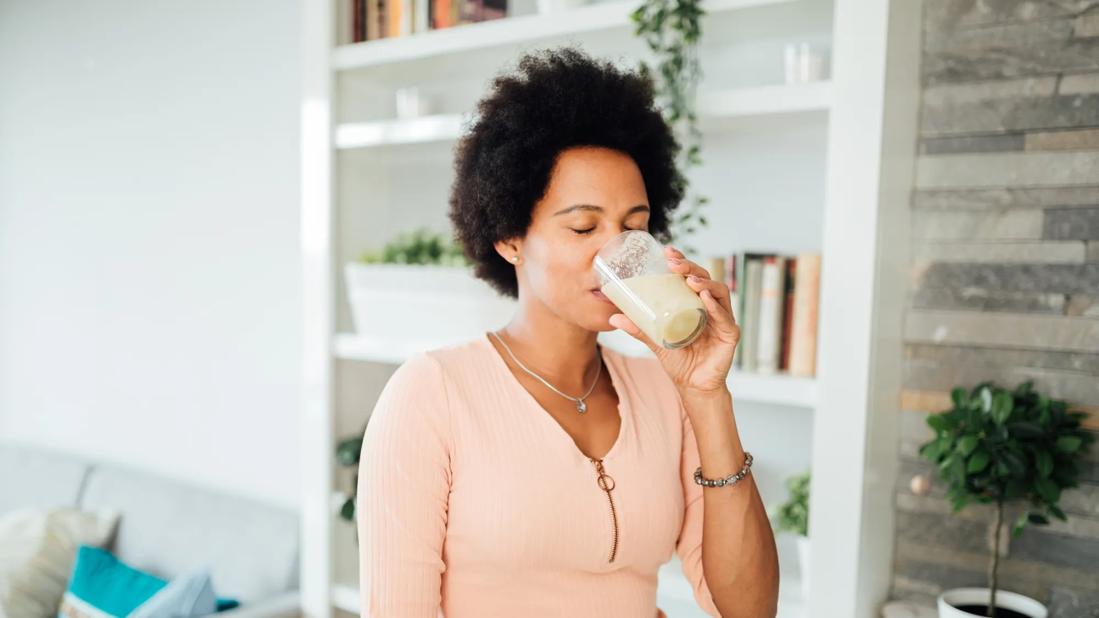 Person drinking a milky smoothie from glass in living room