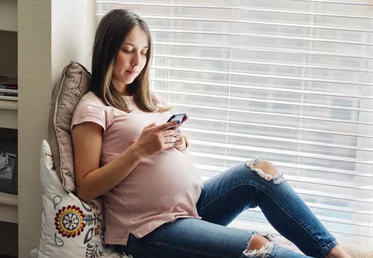 Pregnant woman relaxing in window seat while looking at phone